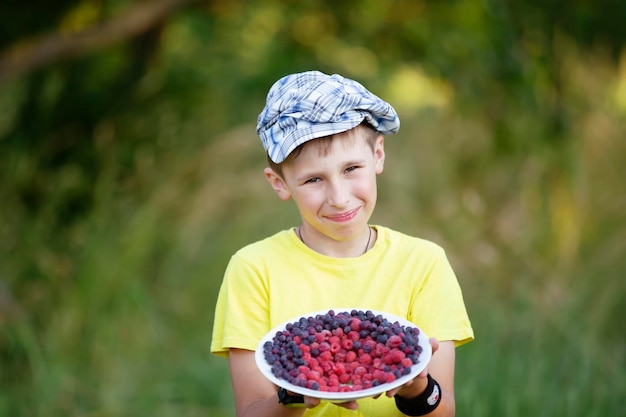 El niño sostiene un plato de fruta El niño cosechó en el jardín