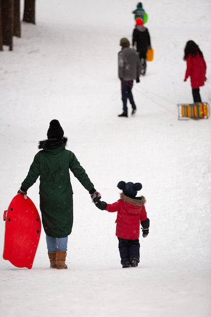 Niño y su madre caminando en un bosque nevado en un día helado de invierno Mamá e hijo bajan la colina
