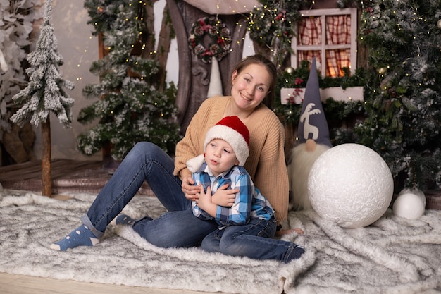 Niño y su madre cerca del árbol de Navidad, casa de juguete y gnomos. Decoración festiva mágica para el hogar.