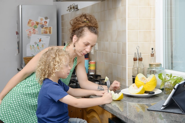Niño y su madre con melón en la cocina