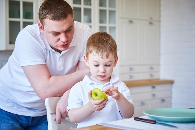 Niño con su padre en la cocina. El niño come una manzana.