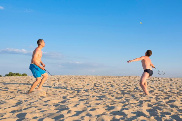 Un niño y su padre juegan bádminton de playa en la orilla del río. concepto de vacaciones de verano