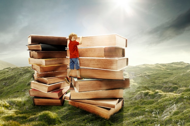 Foto niño subiendo a la torre hecha de grandes libros. sueños de la infancia, concepto de lectura y educación. maravilloso mundo. collage abstracto
