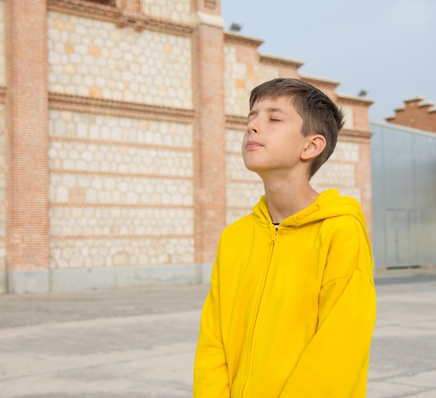 un niño con una sudadera amarilla está de pie frente a un edificio respirando aire fresco