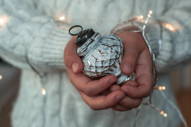 Un niño con un suéter de punto blanco sostiene un juguete de árbol de Navidad vintage blanco en sus manos