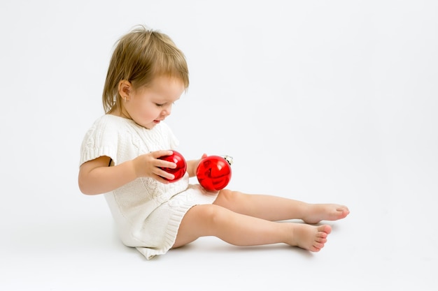 Un niño con un suéter de punto está jugando con dos bolas de Navidad de cristal rojo