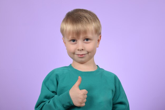 Un niño con un suéter verde está dando un pulgar hacia arriba.