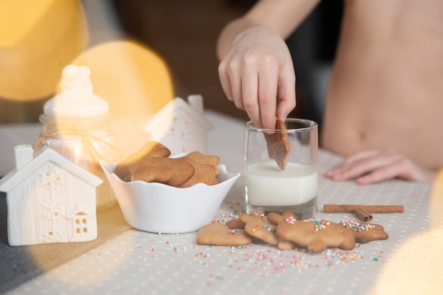 Un niño sumerge galletas de jengibre navideñas en leche sobre una mesa brillante luces bokeh