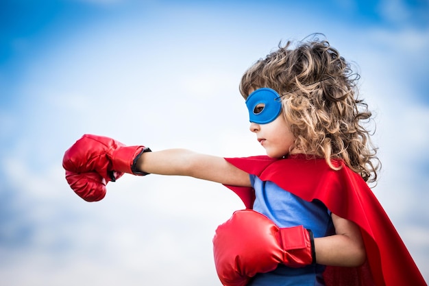 Niño superhéroe contra el fondo de cielo azul dramático