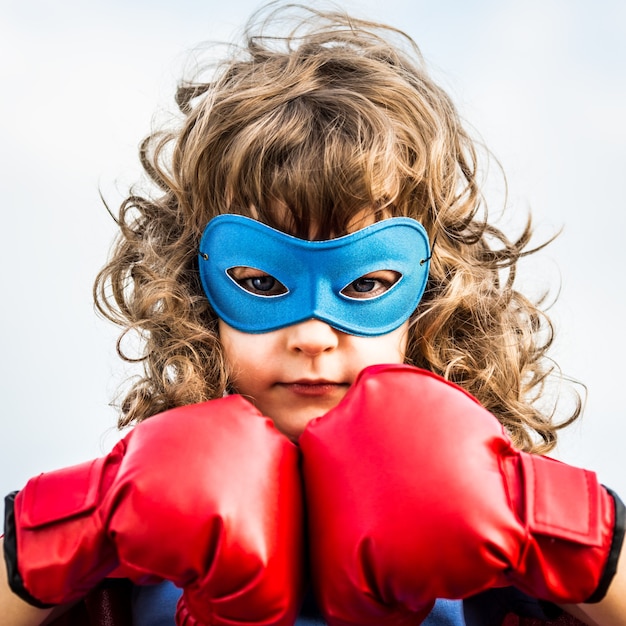 Niño superhéroe con guantes de boxeo sobre fondo de cielo azul. Concepto de feminismo y poder femenino