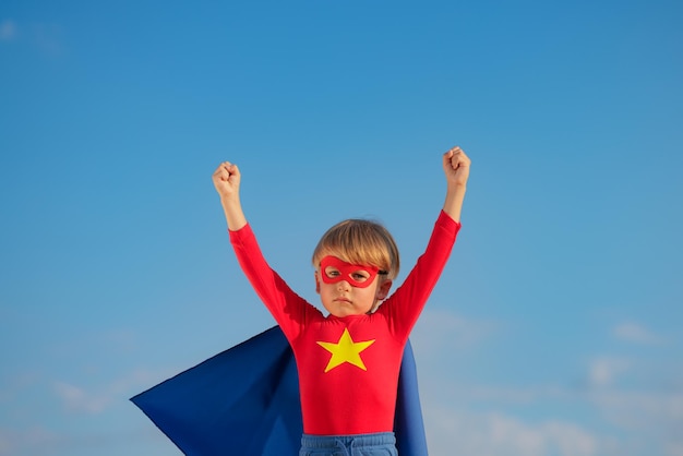 Niño superhéroe jugando al aire libre Niño superhéroe contra el fondo azul del cielo de verano Concepto de imaginación y libertad