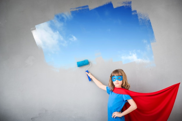 Niño superhéroe pintando la pared de color azul. Niño divirtiéndose en casa. Concepto de renovación de primavera