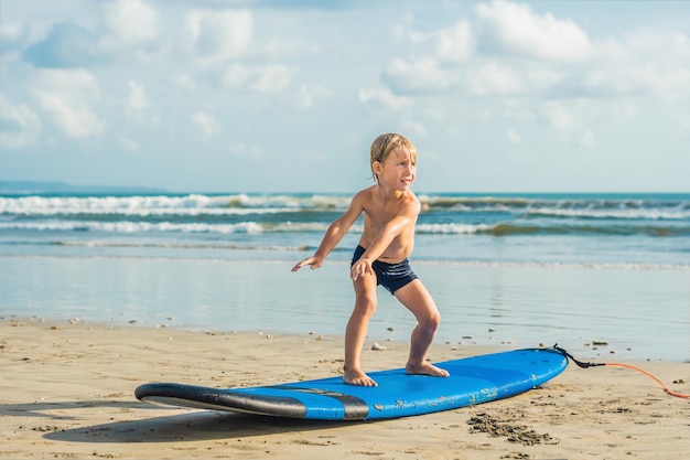Niño surfeando en una playa tropical. Niño en tabla de surf en ola oceánica. Deportes acuáticos activos para niños. Niño nadando con surf. Lección de surf para niños.
