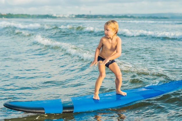 Niño surfeando en una playa tropical. Niño en tabla de surf en ola oceánica. Deportes acuáticos activos para niños. Niño nadando con surf. Lección de surf para niños.