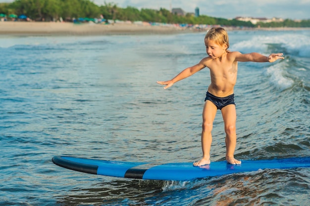 Niño surfeando en una playa tropical. Niño en tabla de surf en ola oceánica. Deportes acuáticos activos para niños. Niño nadando con surf. Lección de surf para niños.