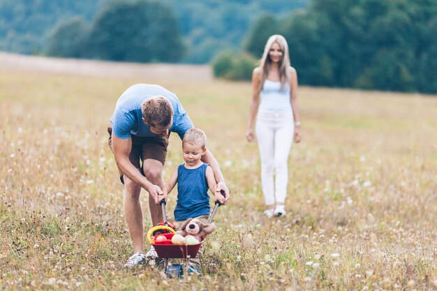 Niño con sus padres empujando un whellbarrow al aire libre