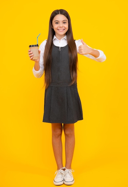 Niño con taza de café o té aislado sobre fondo amarillo de estudio Adolescente con bebida para llevar