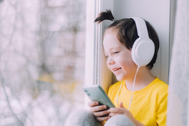 Un niño con un teléfono está sentado en una ventana de estilo de vida Redes sociales Niños modernos Un artículo sobre niños desarrollados