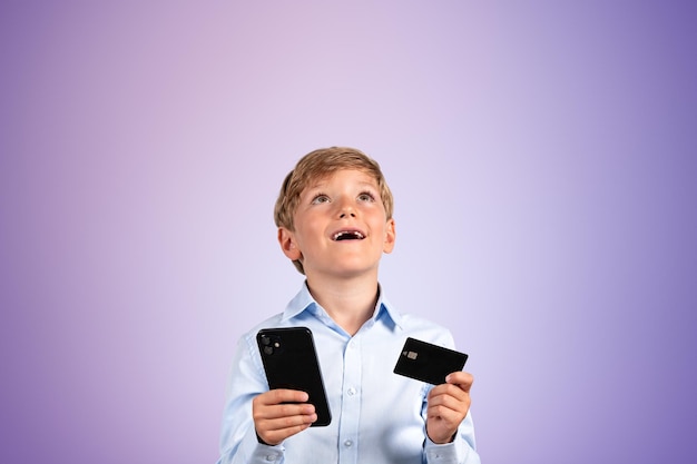 Niño con teléfono inteligente y tarjeta de crédito feliz retrato sobre fondo púrpura vacío