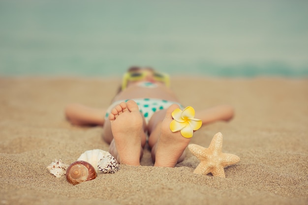 Niño tendido en la arena de la playa con una flor en el pie y conchas y una estrella de mar