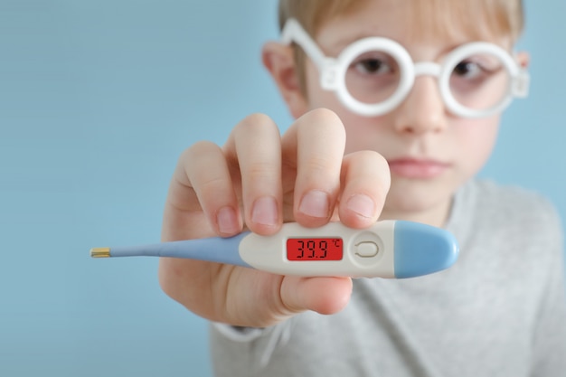 Niño con un termómetro en la mano. Aumento de la temperatura corporal. Cara en la pared