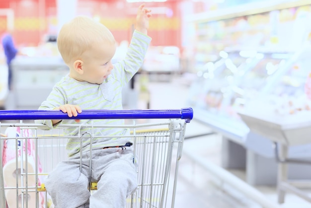 niño en la tienda en el carrito de la compra es un pequeño cliente