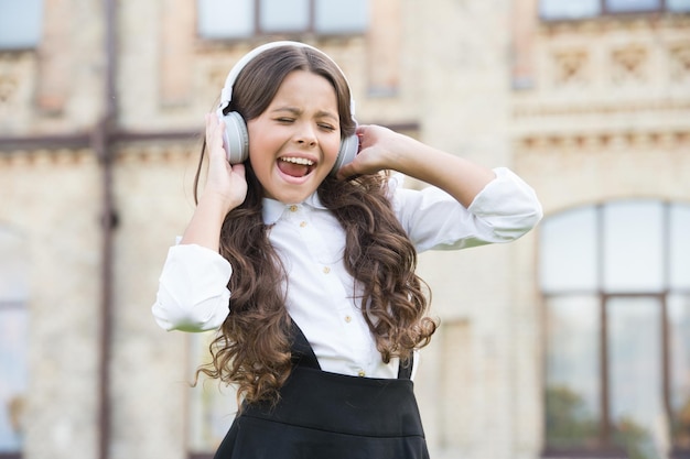 El niño tiene un descanso musical, una niña con auriculares, una niña bonita, usa un uniforme elegante, regreso a la escuela, educación moderna con nueva tecnología, un niño canta en el patio de la escuela y sueña con ser cantante.