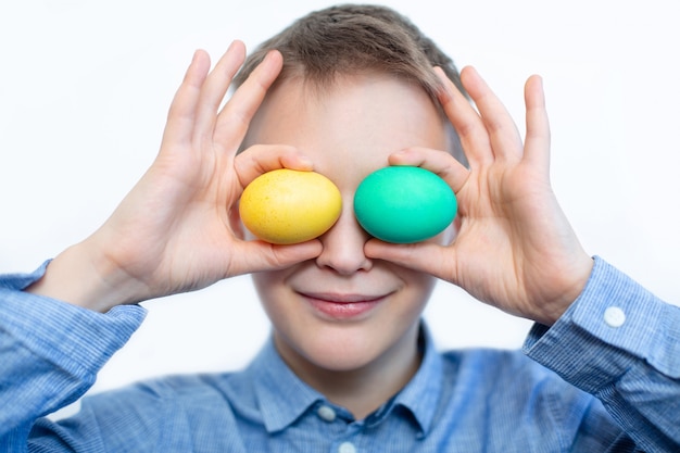 El niño tiene huevos coloridos. Huevo verde y amarillo en manos del niño. Chico alegre tiene huevos cerca de los ojos