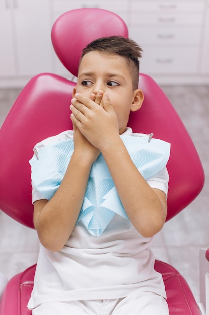 El niño tiene miedo y cierra la boca con las manos en una visita al dentista en la clínica dental.