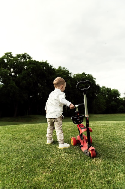 Niño tiene un scooter en sus manos y camina en el parque. transporte ecológico del niño. niño con scooter