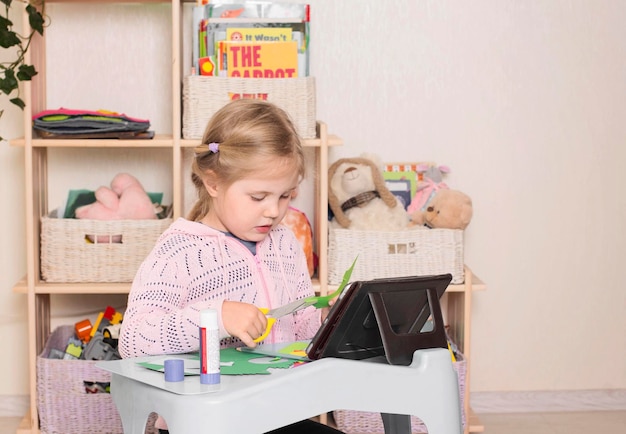 Niño con tijeras y pegamento Retrato de una niña cortando un papel con una tableta