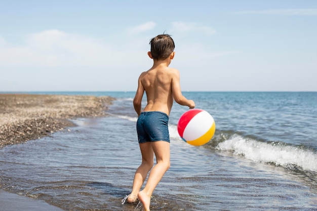 Niño de tiro completo jugando con pelota en la playa