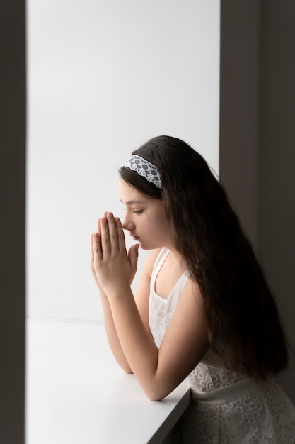 Foto niño de tiro medio rezando en la ventana