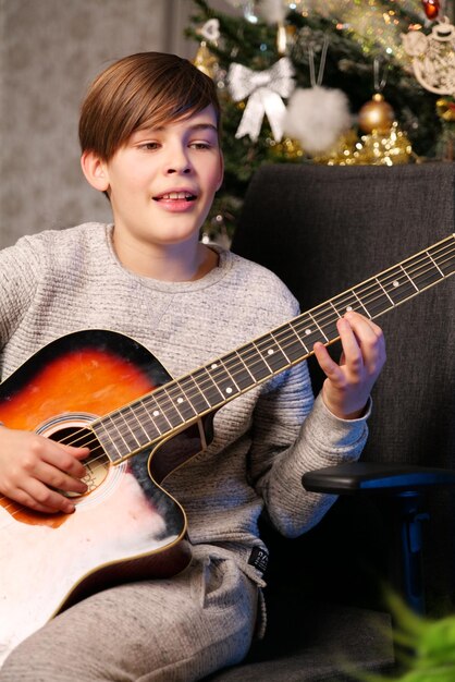 Un niño tocando una guitarra con un árbol de navidad detrás de él.