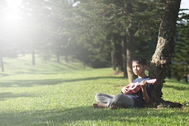 Foto niño tocando la guitarra mientras está sentado en el campo de hierba en el parque