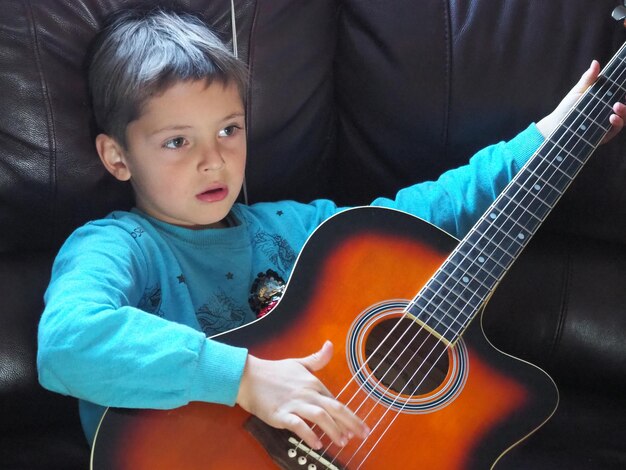 Un niño tocando una guitarra en un sofá.