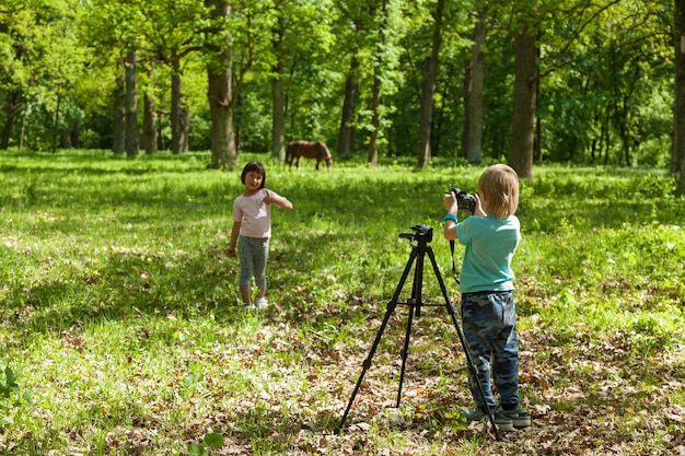 Un niño toma fotografías de una niña en la naturaleza en un parque.