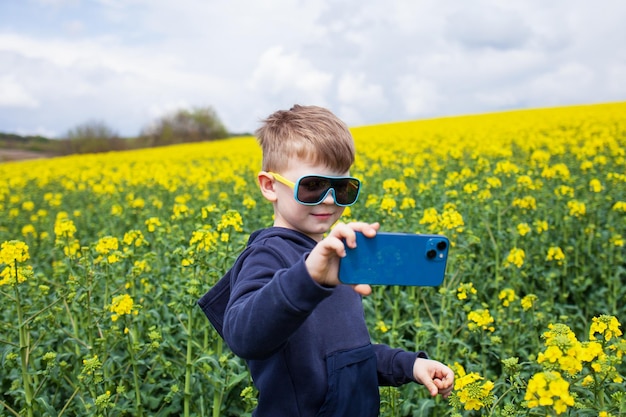 El niño toma fotos del paisaje de verano de canola en un teléfono inteligente