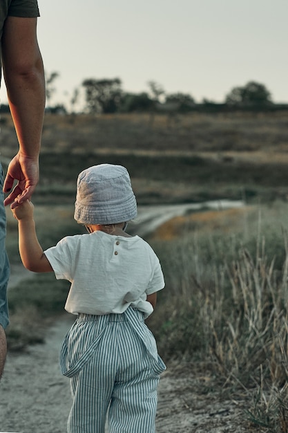 Un niño toma la mano de un adulto y camina por un camino rural.