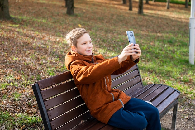 Un niño se toma una selfie con su teléfono mientras está sentado en un banco del parque