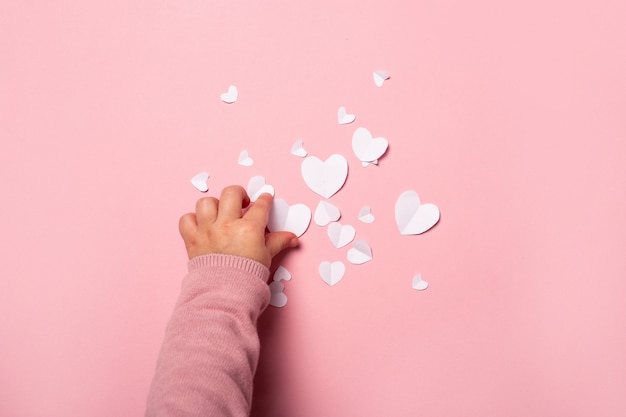 El niño toma una tarjeta de San Valentín de papel sobre un fondo rosa. Composición de San Valentín. Bandera. Vista plana endecha, superior.