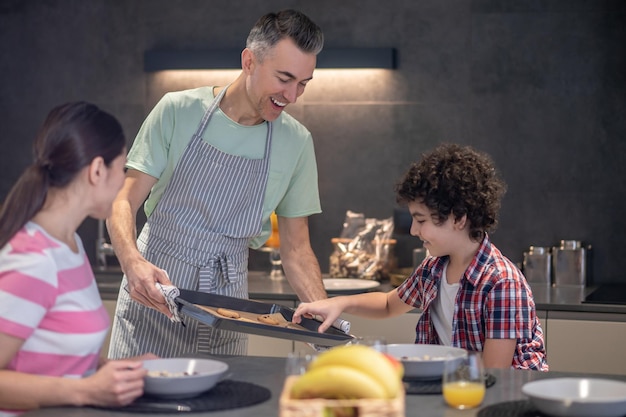 Niño tomando galletas de una bandeja para hornear ofrecida por papá