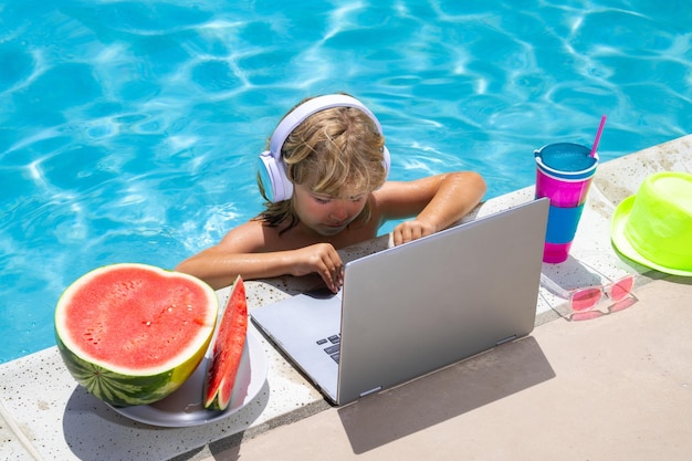 Niño trabajando afuera con una computadora portátil en la piscina Niño trabajando en una computadora portátil desde la piscina Negocios de verano