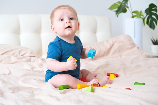 Niño en traje azul jugando con coloridos juguetes ecológicos de madera en la cama