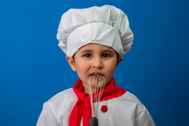 El niño con traje de cocinero. adorable niño con sombrero de chef y delantal sonriendo a la cámara en la cocina. chico con gorro de cocinero