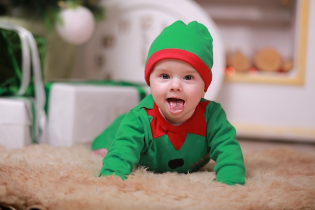 Niño en traje de elfo verde rojo sentado bajo el árbol de Navidad y cajas de regalo.