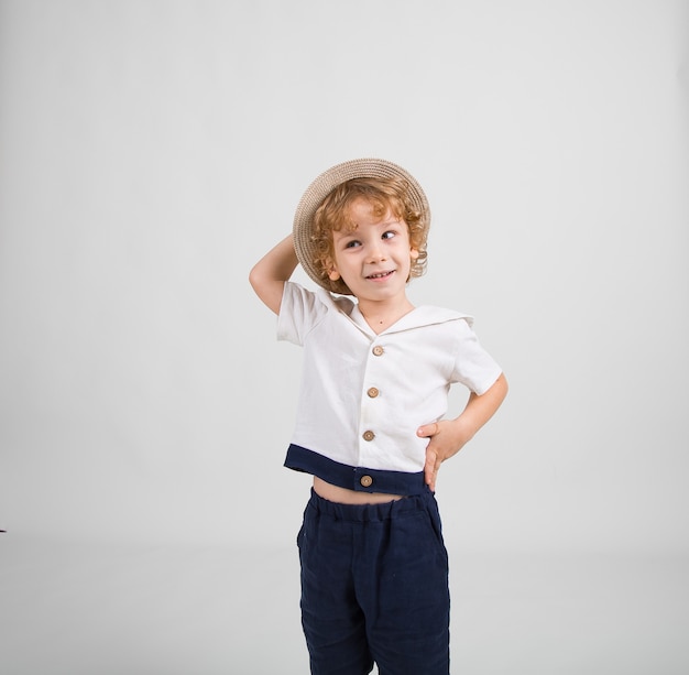 Foto niño en un traje de marinero y un sombrero se encuentra sobre un fondo blanco.