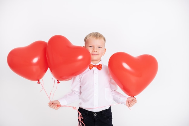 Niño de traje y pajarita roja tiene globos de corazón