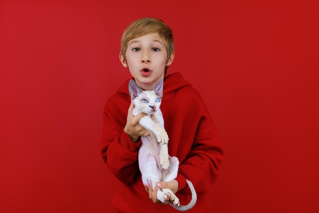 Un niño con un traje rojo sostiene un gatito blanco frente a él y lo muerde juguetonamente para animarlo.