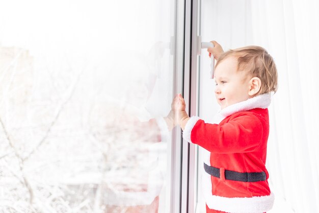 Niño en traje de Santa en el alféizar de la ventana